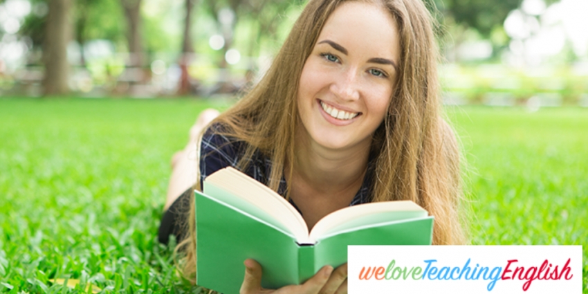 Smiling girl reading and lying on the grass